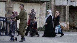 نساء فلسطينيات يمرن بجانب جندي اسرائيلي في مدينة الخليل المنقسمة بالضفة الغربية (فلاش 90)