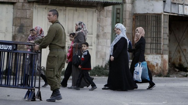 نساء فلسطينيات يمرن بجانب جندي اسرائيلي في مدينة الخليل المنقسمة بالضفة الغربية (فلاش 90)