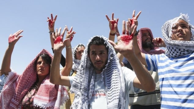 أسرائيليون يلبسون الكوفيات ويرفعون أيديهم الملطخة بالأحمر رمزا للدماء (فلاش 90)