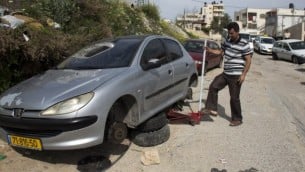 رجل فلسطيني في بيت حنينا يغير إطارات سيارته 24 مارس 2014 بعد أن ثقب من يشتبه بانهم مخربين يهود  إطارات عشرات السيارات الفلسطينية في أحدث ما يسمى "تدفيع الثمن" والتي هي جرائم الكراهية ة ( أ ف ب / أحمد الغرابلي)
