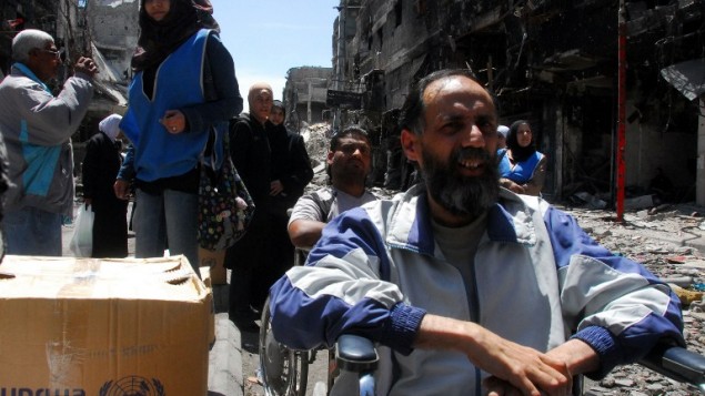 صورة صادرة عن وكالة الانباء السورية الرسمية (سانا) يوم 24 أبريل 2014، لسوريين  ينتظرون صناديق من المساعدات الغذائية التي يتم توزيعها من قبل وكالة إغاثة الأمم المتحدة (الأونروا) في مخيم للاجئين الفلسطينيين اليرموك جنوب سوريا . AFP PHOTO / HO / SANA