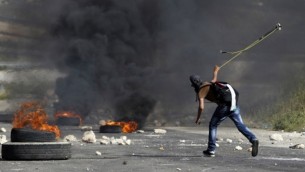 متظاهر فلسطيني ملثم يستخدم مقلاع لالقاء حجر على قوات الأمن الإسرائيلية خارج سجن عوفر في الضفة الغربية قرية بيتونيا،  16 مايو 2014 ( AFP / عباس المومني).