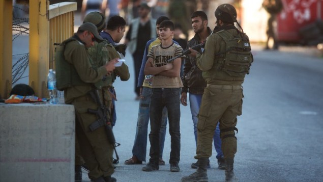 جندي إسرائيلي يتفحص هوية شاب فلسطيني عند نقطة تفتيش في بلدة الخليل بالضفة الغربية،  15 يونيو 2014، AFP PHOTO / مناحيم كاهانا