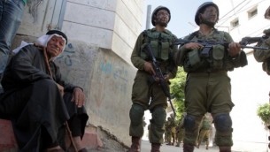 رجل فلسطيني يجلس بجانب الطريق بينما يقف جنديان اسرائيليان في القرية الفلسطينية تفوح غربي الخليل 18, 2014 AFP/HAZEM BADER