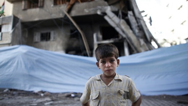 طفل فلسطيني يقف أمام القماش المشمع الملفوف حول مبنى دمر في أعقاب ضربة جوية اسرائيلية  14 يوليو  2014 في مدينة غزة.  AFP PHOTO / THOMAS COEX