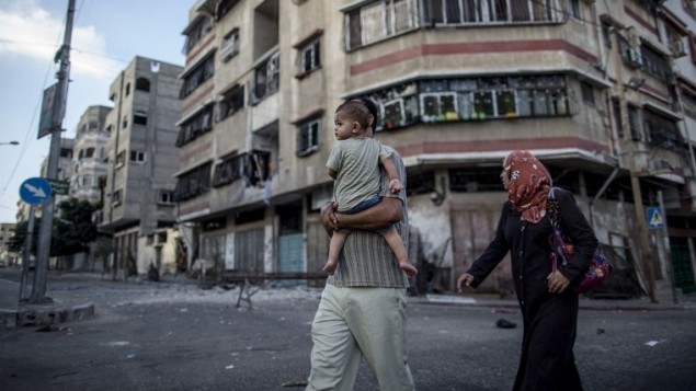 عائلة فلسطينية تمشي بين الانقاض من مبنى في وسط مدينة غزة  25 يوليو 2014.  AFP PHOTO / MARCO LONGARI