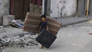 صبي فلسطيني يمشي وسط الحطام في شارع مهجور في وسط مدينة غزة، ويحمل فراش  في محاولة لانقاذ ما تبقى من الشقة المهدومة عائلته22 يوليو 2014.  AFP PHOTO / MOHAMMED ABED
