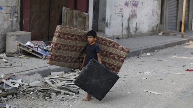 صبي فلسطيني يمشي وسط الحطام في شارع مهجور في وسط مدينة غزة، ويحمل فراش  في محاولة لانقاذ ما تبقى من الشقة المهدومة عائلته22 يوليو 2014.  AFP PHOTO / MOHAMMED ABED