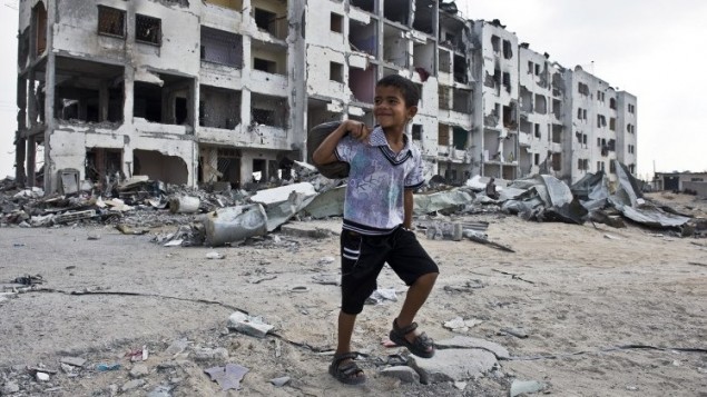 الصبي الفلسطيني يوسف، 8، يبتسم لأنه يدرك انه يتم تصويره بالقرب من المباني السكنية المهدمة وهو يحمل الخبز  إلى والده  14 أغسطس 2014 في بيت حانون، شمال قطاع غزة.  عائلة يوسف تقضي ايامها ولياليها في مدرسة للأمم المتحدة. AFP PHOTO / ROBERTO SCHMIDT