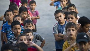 أطفال فلسطينيون  في ساحة مدرسة للأمم المتحدة، خلال النشاط الصباحي وكان من المفترض أن تبدأ الدراسة في مدينة غزة  24 أغسطس 2014. AFP PHOTO / ROBERTO SCHMIDT