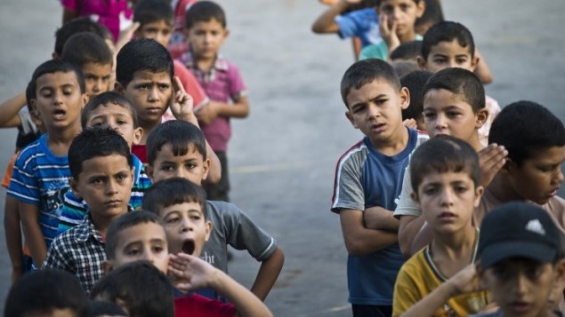 أطفال فلسطينيون  في ساحة مدرسة للأمم المتحدة، خلال النشاط الصباحي وكان من المفترض أن تبدأ الدراسة في مدينة غزة  24 أغسطس 2014. AFP PHOTO / ROBERTO SCHMIDT