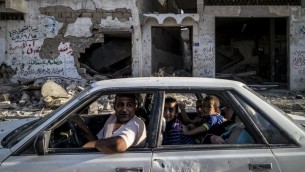أسرة فلسطينية تسوق عبر حارة مهدمة امام مبنى مدمر في حي الشجاعية  مدينة غزة 6 أغسطس 2014.  AFP PHOTO / MARCO LONGARI
