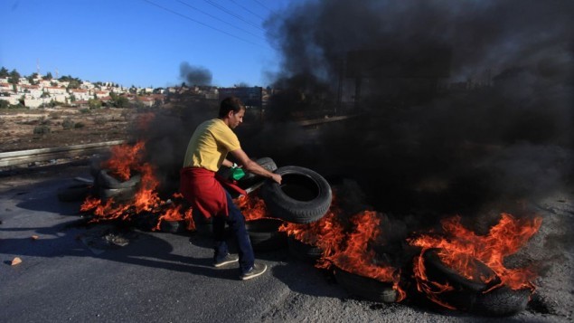 شاب فلسطيني من مخيم الجلزون للاجئين يضع إطارات مشتعلة على الطريق المؤدي إلى مستوطنة بيت إيل بالقرب من رام الله خلال اشتباكات مع جنود إسرائيليين، 24 أكتوبر، 2014. (STR/Flash90) شاب فلسطيني من مخيم الجلزون للاجئين يضع إطارات مشتعلة على الطريق المؤدي إلى مستوطنة بيت إيل بالقرب من رام الله خلال اشتباكات مع جنود إسرائيليين، 24 أكتوبر، 2014. (STR/Flash90)