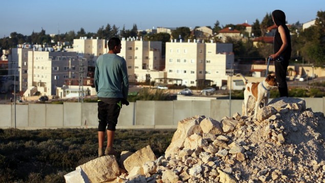 صورة توضيحية، اطفال فلسطينون من مخيم الجلزون للاجئين يطلون من وراء الجدار على مستوطنة بيت ايل، في الضفة الغربية 7 أبريل، 2015. AFP PHOTO/ABBAS MOMANI