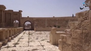 صورة لآثار تدمر مع ما يبدو كمقاتل من تنظيم الدولة الإسلامية في الخلفية، صورة شاشة لشريط اصدره تنظيم الدولة الإسلامية في 27 مايو 2015 (YouTube)