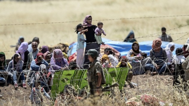 صورة مأخوذة من الجانب التركي للحدود في سوروك، محافظة سانليورفا، تظهر الجنود الأتراك وهم يحرسون الحدود في الوقت الذي ينتظر فيه أكراد سوريون وراء  السياج الشائك على الجانب السوري من الحدود بعد فرارهم من مدينة كوباني السورية، المعروفة أيضا بعين العرب، 26 يونيو، 2015.  (AFP PHOTO/BULENT KILIC)