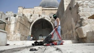 شاب فلسطيني ملثم يضع عصابة رأس تحمل شعار حركة حماس يقوم بإخراج بساط محترق من مسجد الأقصى في البلدة القديمة في القدس خلال مواجهات في الموقع قي 13 سبتبمر، 2015، ساعات قليلة فقط قبل بدء الإحتفالات بالسنة العبرية الجديدة، 13 سبتبمر، 2015. (AFP PHOTO/AHMAD GHARABLI)