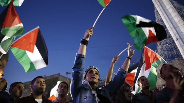 فلسطينيون يلوحون بالعلم الفلسطيني في رام الله بينما يشاهدون بثا مباشرا لرفع العلم الفلسطيني امام مقر الأمم المتحدة في نيويورك، 30 سبتمبر2015 (ABBAS MOMANI / AFP)