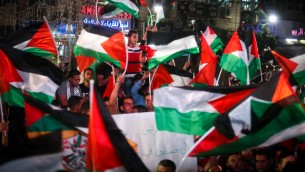 فلسطينيون يلوحون بالعلم الفلسطيني في رام الله بينما يشاهدون بثا مباشرا لرفع العلم الفلسطيني امام مقر الأمم المتحدة في نيويورك، 30 سبتمبر2015 (FLASH90)