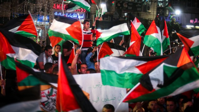 فلسطينيون يلوحون بالعلم الفلسطيني في رام الله بينما يشاهدون بثا مباشرا لرفع العلم الفلسطيني امام مقر الأمم المتحدة في نيويورك، 30 سبتمبر2015 (FLASH90)