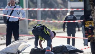 شرطي إسرائيلي يقف بجانب جثة منفذ هجوم فلسطيني الذي قُتل بعد إطلاق النار عليه بعد أن قام بطعن حارسي أمن إسرائيليين في منطقة بركان الصناعية  القريبة من مستوطنة أريئيل، 24 ديسبمر، 2015. (Phot by AFP Photo/Jack Guez)