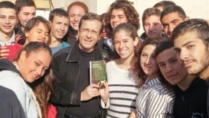 رئيس المعارضة يتسحاك هرتسوغ يتصور مع نسخة من كتاب ’جدار حي’ للكاتبة دوريت رابينيان، محاط بطلاب في الكلية السابقة للجيش في سديروت، 31 ديسمبر 2015 (Courtesy Zionist Union)