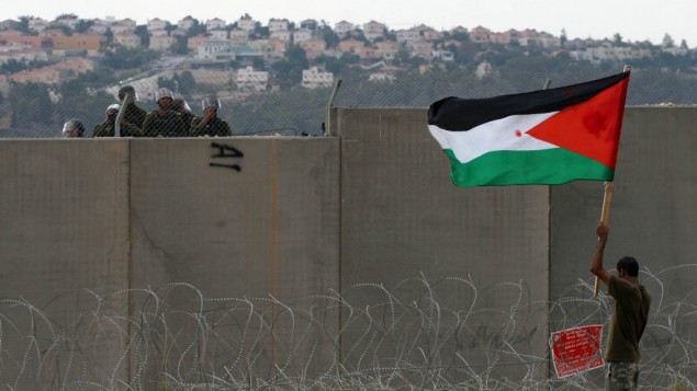 متظاهر فلسطيني يحمل علم بينما يقف بالقرب من الجدار الأمني خلال مظاهرة في بلعين، سبتمبر 2011 (Issam Rimawi/Flash90)
