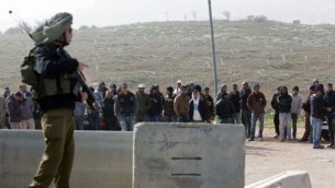 جندي إسرائيلي يقف بالقرب من عمال فلسطينيين تم إخراجهم من مستوطنة تقوع جنوبي القدس في أعقاب هجوم وقع فيها في 18 يناير، 2016. (AFP / MENAHEM KAHANA)