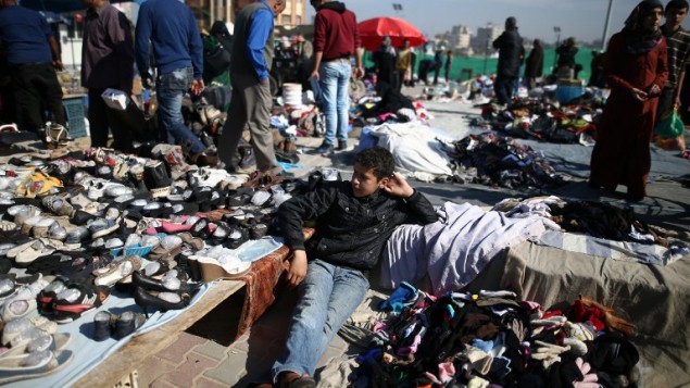 شاب فلسطيني يجلس بين الملابس المستخدمة في سوق البالية الاسبوعي في مخيم نصيرات، في مركز قطاع غزة، 29 فبراير 2016 (MOHAMMED ABED / AFP)
