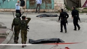 جنود إسرائيليون والشرطة يحيطون بجثتي منفذي هجوم فلسطينيين قُتلا بعد أن هاجما جندي إسرائيلي بسكين مما أدى إلى إصابته قبل أن يُقتلا بنيران الوقوات الإسرائيلية، بحسب متحدث بإسم الجيش، عند مدخل حي تل الرميدة في مدينة الخليل بالضفة الغربية، 24 مارس، 2016. (AFP / HAZEM BADER)