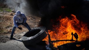 متظاهر فلسطيني يشعل إطار سيارة خلال مواجهات في الضفة الغربية، 5 ديسمبر 2015 (FLASH90)