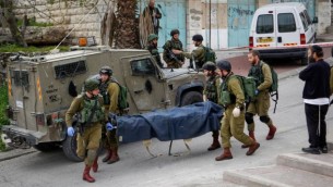 جنود إسرائيليون ينقلون جثة شاب فلسطيني قُتل جراء إطلاق النار عليه بعد أن قام بطعن جندي في مدينة الخليل بالضفة الغربية، 24 مارس، 2016. (Wissam Hashlamon/Flash90)
