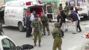 جندي إسرائيلي يمر بجانب منفذ الهجوم الفلسطيني منزوع السلاح والملقى على الأرض قبل لحظات من قيام جندي آخر بإطلاق النار عليه في الرأس بعد هجوم طعن في الخليل في 24 مارس، 2016. (لقطة شاشة: بتسيلم)