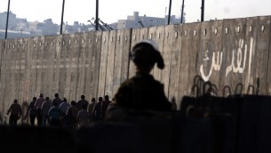 جندي اسرائيلي يراقب فلسطينيين يمرون حاجز قلنديا متجهين نحو القدس (Issam Rimawi/Flash90)