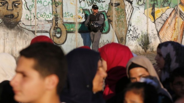شرطي حدود اسرائيلي يراقب بينما يمر فلسطينيين عبر حاجز قلنديا في الضفة الغربية بطريقهم الى ثاني صلاة جمعة خلال شهر رمضان، 17 يونيو 2016 (AFP /ABBAS MOMANI)