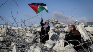 والدة مراد ادعيس، منفذ هجوم فلسطيني، تحمل العلم الفلسطيني خلال وقوفها على على أنقاض منزل العائلة بعد أن قام الجيش الإسرائيلي بهدمه في قرية يطا، جنوبي الخليل، في 11 يونيو، 2016. دعيس قام بقتل دفنا مئير، الأم لستة أطفال، بعد طعنها.