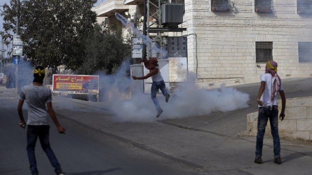 شبان فلسطينيون ملثمون يلقون قنابل غاز باتجاه عناصر شرطة الحدود خلال اشتباكات في بلدة الرام في الضفة الغربية، 22 اكتوبر 2015 (AFP Photo/Abbas Momani)