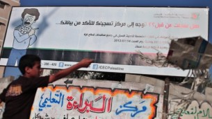 فتى فلسطيني يقف إلى جانب لوحة إنتخابات في غزة. (Wissam Nassar/Flash90)
