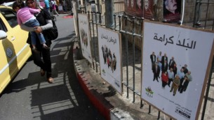 سيدة فلسطينية تحمل طفلها تمر من أمام ملصقات للحملة الإنتخابية في رام الله في اليوم الأول من الحملة الإنتخابية للإنتخابات المحلية في 6 أكتوبر، 2012. (Issam Rimawi/Flash90)