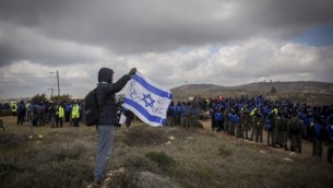 شاب يحمل علما إسرائيليا في الوقت الذي احتشدت فيه القوات الإسرائيلية استعدادا لإخلاء بؤرة عامونا الإستيطانية الغير قانونية، 1 فبراير، 2017. (Miriam Alster/Flash90)