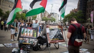 سياح إسرائيليون يقفون أمام منصة لحركة المقاطعة وسحب الإستثمارات وفرض العقوبات مع صورة وأعلام فلسطينية، في دام سكوير وسط أمستردام، هولندا، 24 يونيو، 2016. (Hadas Parush/Flash90)