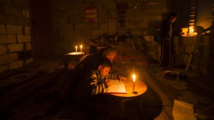 امرأة فلسطينية تساعد ابنها على الدراسة على ضوء شمعة في مخيم خان يونس، شمال قطاع غزة، 19 ابريل 2017 (AFP/MAHMUD HAMS)