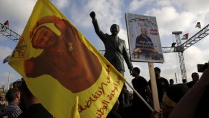 متظاهرون يحملونم صورا لمروان البرغوثي أمام تمثال نيلسون مانديلا في مدينة رام الله في الضفة الغربية، 3 مايو، 2017، خلال تظاهرة تضامن مع الأسرى الفلسطينيين في السجون الإسرائيلية. (AFP/ABBAS MOMANI)