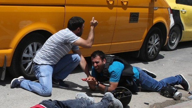 صحفي فلسطيني مصاب بجانب جثمان رجل قال مسؤولون فلسطينيون انه قُتل على يد مستوطن اسرائيلي خلال اشتباكات بالقرب من حاجز حوارة في الضفة الغربية، 18 مايو 2017 (AFP PHOTO / JAAFAR ASHTIYEH)