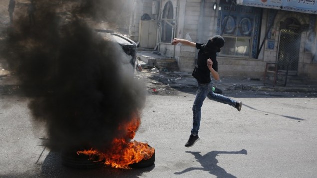فلسطيني ملثم يرشق الحجارة  خلال اشتباكات مع جنود اسرائيليين بعد مظاهرة دعم للاسرى الفلسطينيين المضربين عن الطعام في السجون الإسرائيلية وايضا لإدانة زيارة الرئيس الامريكي دونالد ترامب لإسرائيل والاراضي الفلسطينية في حاجز قلنديا، 22 مايو 2017 (ABBAS MOMANI / AFP)