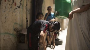 طفل فلسطيني يقوم بتبريد نفسه بماء من صفيحة يحملها رجل خلال موجة حر في مخيم الشاطئ في مدينة غزة، 2 يوليو، 2017. (AFP PHOTO / Mahmud Hams)