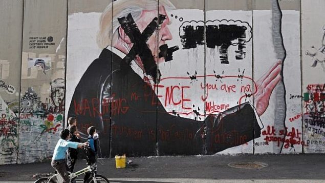 أطفال فلسطينيون ينظرون إلى رسم غرافيتي للرئيس الأمريكي دونالد ترامب وشعارات ضد نائب الرئيس مايك بنس على الجدار الفاصل الإسرائيلي في مدينة بيت لحم في الضفة الغربية خلال مواجهات بين محتجين فلسطينيين والقوات الإسرائيلية عند حاجز إسرائيلي، 7 ديسمبر، 2017. (AFP/Thomas Coex)