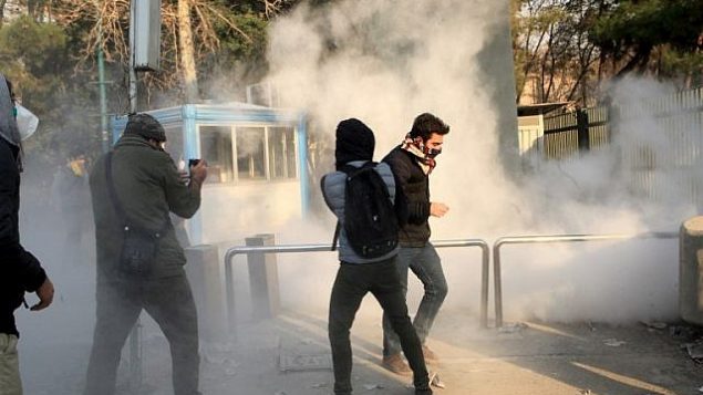 طلاب إيرانيون يحتمون من الغاز المسيل للدموع في جامعة طهران خلال مظاهرة بدافع الغضب على المشاكل الاقتصادية في العاصمة طهران في 30 ديسمبر 2017. (STR/AFP)