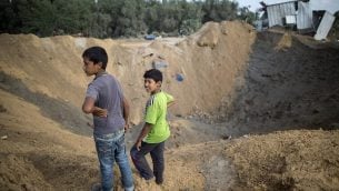 صورة توضيحية: يقف أطفال فلسطينيون بالقرب من حفرة في بيت لاهيا في شمال قطاع غزة في 22 أغسطس / آب 2016، بعد غارة جوية إسرائيلية استهدفت مواقع حماس ردا على صاروخ أطلق من القطاع الذي ضرب مدينة سديروت الإسرائيلية. (Mahmud Hams/AFP)