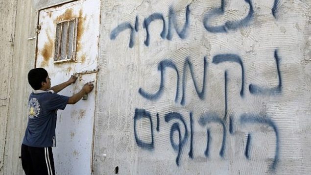 صورة توضيحية: صبي فلسطيني يفتح الباب بعد أن كتب على الجدران بالعبرية، ويزعم أن المستوطنون اليهود قاموا بذلك، في قرية عقربة في الضفة الغربية، بالقرب من مدينة نابلس، في 2 يوليو / تموز 2014. (AFP/JAAFAR ASHTIYEH)